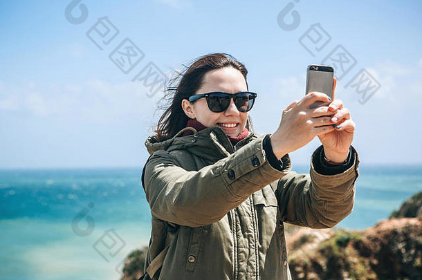 一个积极的旅游女孩可以欣赏美丽的风景，或者自拍，或者用手机在线与人交流。