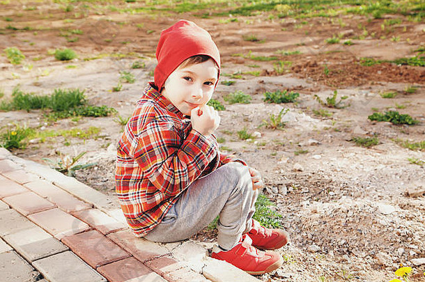 男孩穿红色的他夹克运动鞋坐着公园阳光明媚的一天