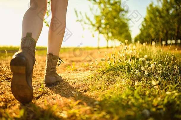 阳光明媚的日子里，路旁<strong>绿色果园</strong>中行走女孩的腿和鞋。
