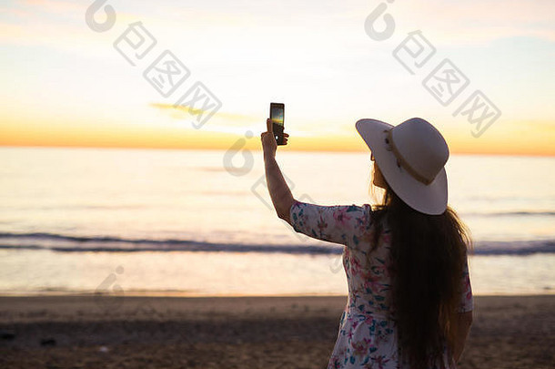 年轻女子在度假旅行时，用<strong>手机</strong>或智能<strong>手机数码</strong>相机拍摄大海和日落，并将其上传到网上。