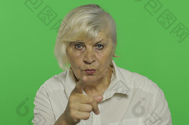 一位老妇人指着摄像机笑了。穿着白衬衫的漂亮老奶奶。放置您的徽标或文字。色度键。绿色屏幕背景