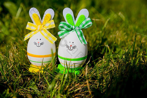 以绿色草地为背景，以复活节彩蛋为复活节兔子的可<strong>爱创意</strong>照片。复活节快乐贺卡。兔子复活节彩蛋。复活节假期概念与两个可爱的手工鸡蛋：兔子