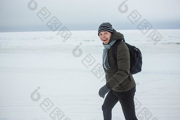 快乐的高加索人在积雪覆盖的海岸上徒步旅行。他用舌头展示出滑稽的面部表情，表达出冬季乐趣、假期、健康生活方式的理念。
