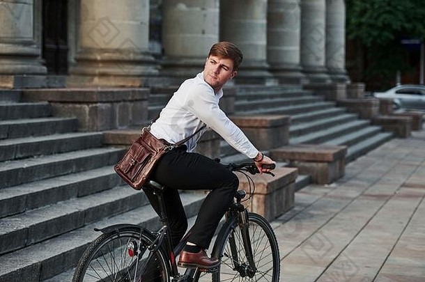 年轻而成功。穿着正装、骑着黑色自行车的商人在城里