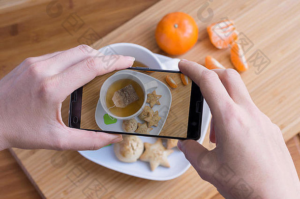 女人用手机拍茶早餐和橘子