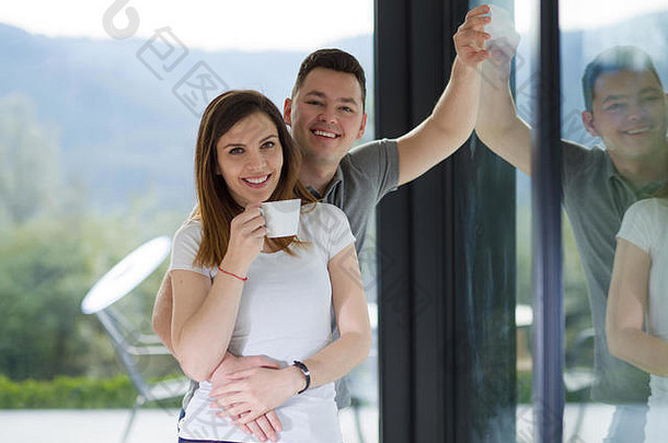 浪漫快乐的年轻夫妇在他们豪华的家里靠窗享受着早晨的咖啡