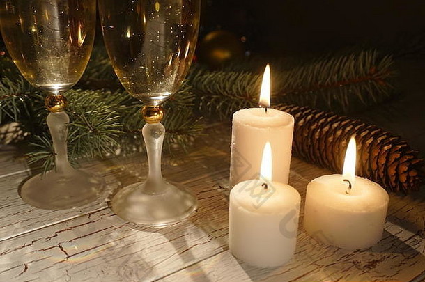 在圆锥体的背景下，champahne玻璃杯附近的三支发光蜡烛构成了浪漫的新年。
