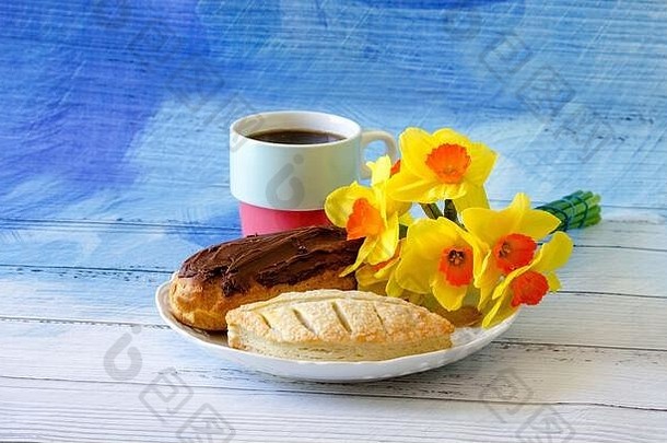 盘子里放着精美的糕点，上面装饰着一束鲜艳的水仙花和一个装满咖啡的五颜六色的杯子