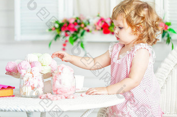 可爱的卷曲的女孩粉红色的衣服花边波尔卡点坐着表格花园吃糖果
