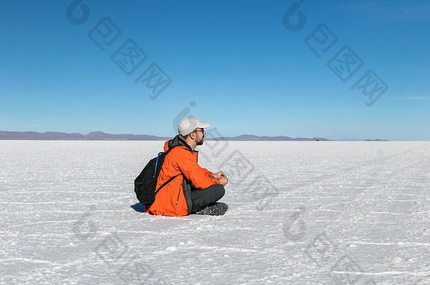 年轻的时髦男人坐在乌尤尼盐滩沙漠的瑜珈姿势中，看着别处。玻利维亚的旅游度<strong>假景观</strong>与空间