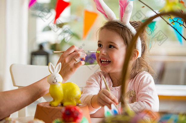 一对母女在庆祝复活节，用黄色的画笔画兔子。幸福的家庭微笑着，笑着。可爱的小女孩在兔耳朵