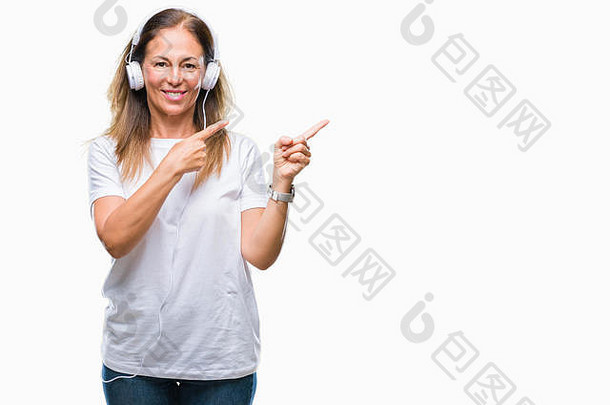 中年西班牙裔妇女戴着耳机在孤立的背景下听音乐，微笑着看着摄像机，双手和手指指着镜头