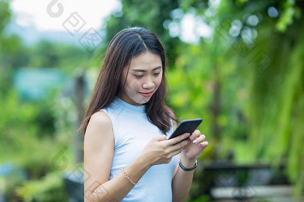 亚洲女孩在花园里用手机和短信放松