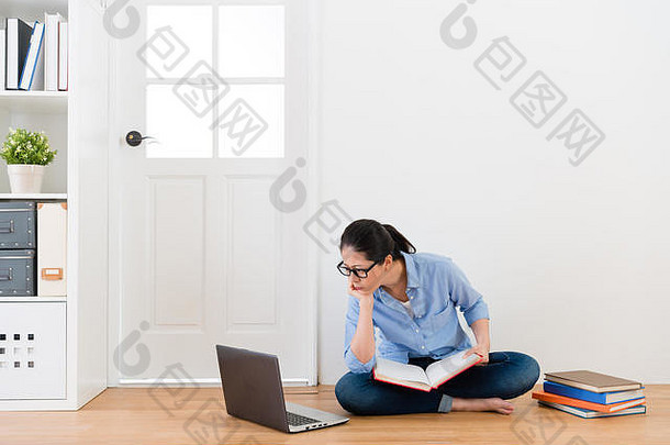 年轻漂亮的女学生坐在白色背景的木地板上，使用移动电脑学习，感到困惑。