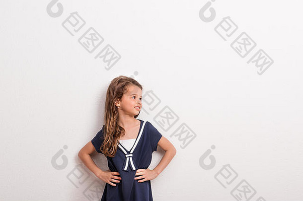 摄影棚里一个小女孩的肖像，白色背景，双手放在臀部。