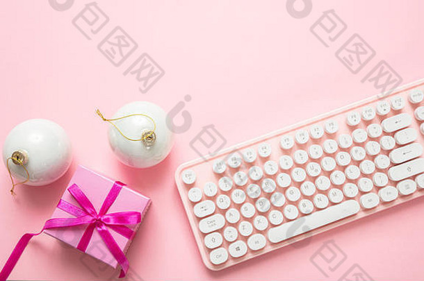 粉红色的圣诞办公室。圣诞球、礼物和电脑键盘，粉色背景，俯视图