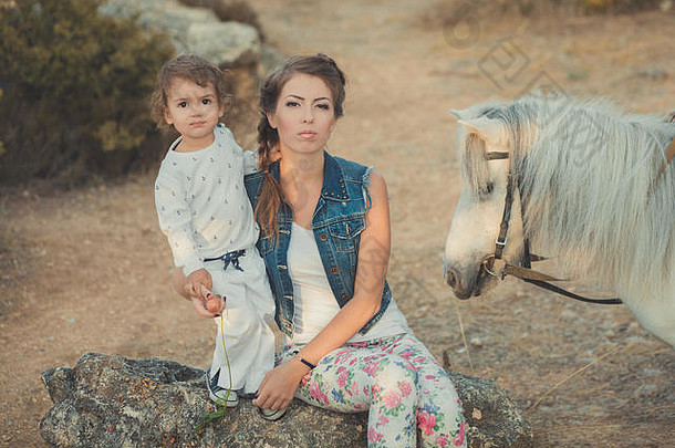 浪漫的场景美丽的女士年轻的母亲和她可爱的小女儿一起在城中村公园散步喂养白马小马。