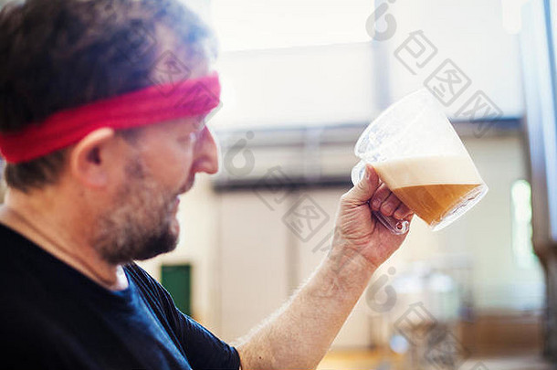 一个拿着红色手帕的酿酒师拿着一壶正在酿造的啤酒并检查它。