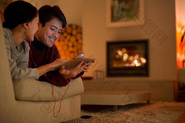 戴着耳机的幸福夫妇在客厅沙发上共享数字平板电脑