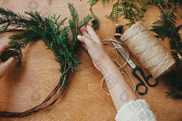 手拿着杉木树枝和松果、线、剪刀放在木桌上。制作质朴的圣诞花环。c的车间详情