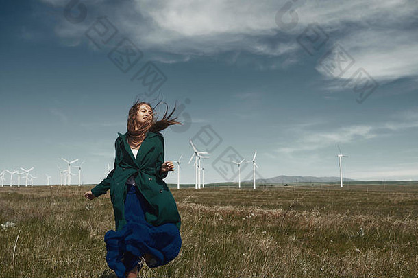 一个头发蓬乱的女人站在风机旁随风飘动