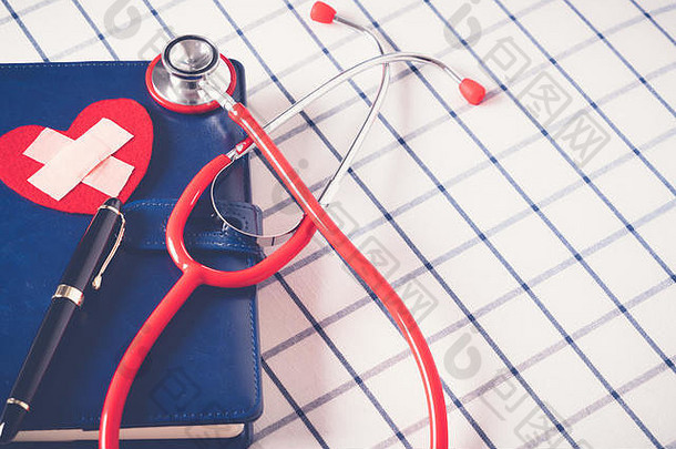 世界卫生日医疗保健和医疗概念蓝色每日笔记本上的红色听诊器和红色心形