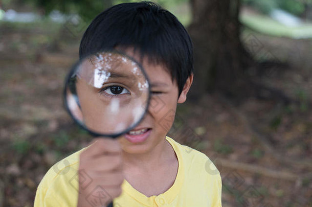 年轻的亚洲男孩透过放大镜观看。教育理念