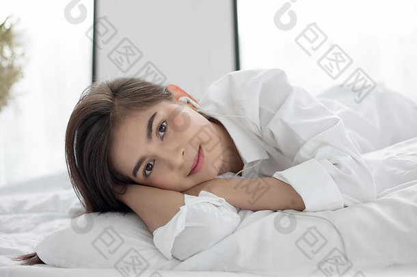 亚洲女人微笑感觉无忧无虑的说谎床上早....醒着的年轻的美丽的女孩听音乐耳机
