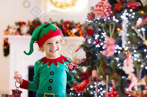 孩子在家里装饰圣诞树。小男孩穿着精灵服装，戴着圣诞装饰的帽子。一家人带着孩子庆祝寒假。儿童装饰