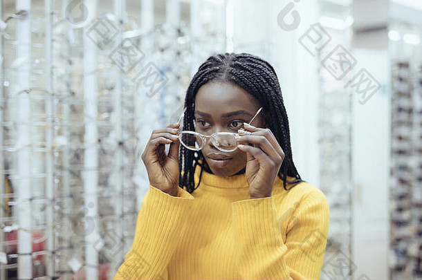 年轻的非洲美女在眼镜店挑选眼镜架。可爱的女孩决定戴不同形状和颜色的眼镜