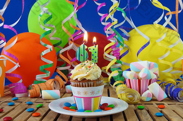 <strong>61</strong>生日纸杯蛋糕，蜡烛在乡村木桌上燃烧，背景是五颜六色的气球，背景是蓝色墙上的塑料杯糖果