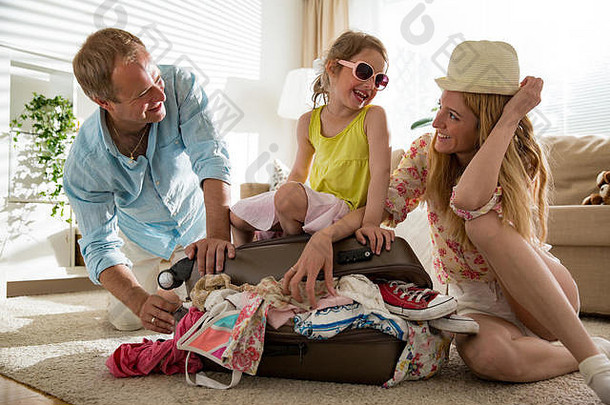 幸福的一家人穿着五颜六色的夏装，把衣服装在员工的手提箱里。小女孩坐在行李袋上，准备旅行。