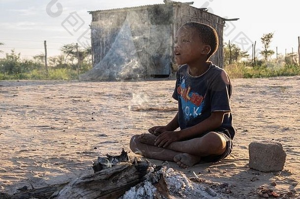 纳米比亚Nyae Nyae的Deng//e村，黎明时分，一名年轻的Ju/hoansi男孩坐在火炉旁