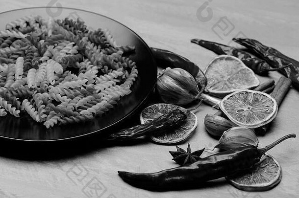 美味多彩的意大利面食，黑色陶瓷盘，辣椒，橙色，大蒜，八角和肉桂，灰色纹理背景，侧视图