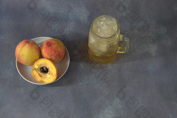 成熟多汁的桃子放在陶瓷盘子上，一杯桃汁加冰块，灰色抽象背景。