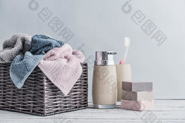 饮水机、肥皂条、牙刷和毛巾放在一个柳条篮中，背景为浅色