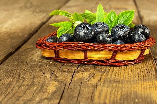 把蓝莓放在一个小柳条篮子里。在木桌<strong>上新</strong>采摘的森林水果。蓝莓的销售。健康<strong>夏日</strong>点心