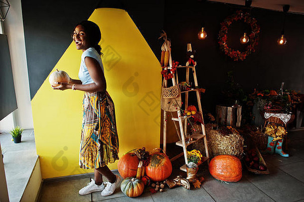 非洲裔美国女孩拿着南瓜反对秋意装饰。非洲的秋天。