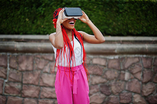 时尚的非裔美国女商人，穿着粉色裤子，戴着虚拟现实眼镜，穿着红色恐惧服。