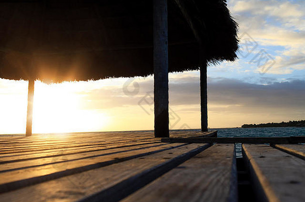日落或日出时海滩上木质露台的特写镜头。背景是清晨有棕榈树和蓝色海水的海滨。五彩