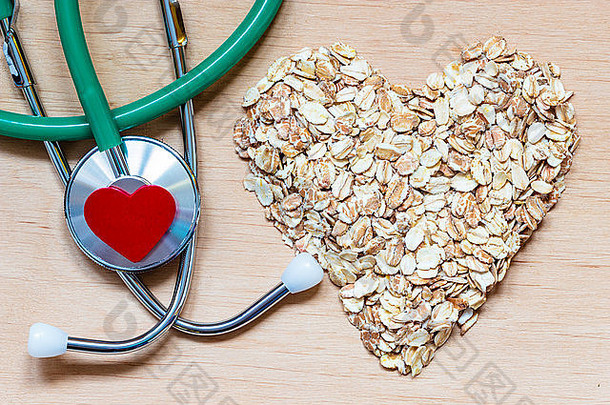 饮食保健概念。燕麦麦片心形，木制表面听诊器。降胆固醇健康食品