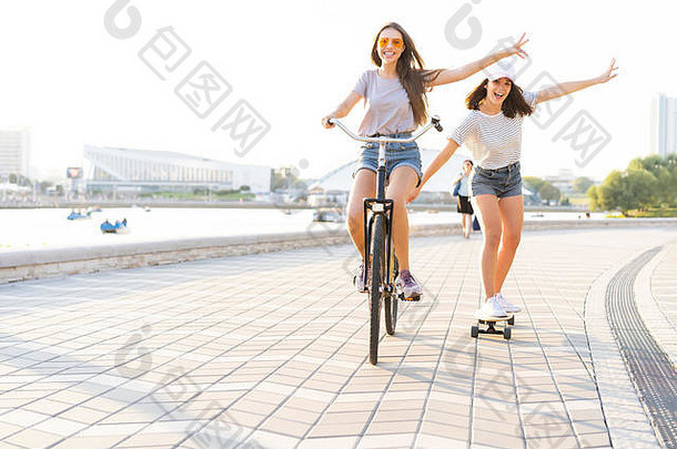 穿着牛仔裤、短裤、骑自行车的可爱笑脸年轻女子拉着女孩玩滑板