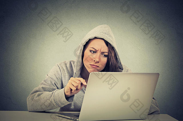 坐在灰色墙壁背景上的<strong>笔记本电脑</strong>前的年轻紧张不安的女人。负面表情情绪问题