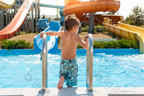夏天，健康的小孩带着水管滑梯进入水上公园的蓝色游泳池