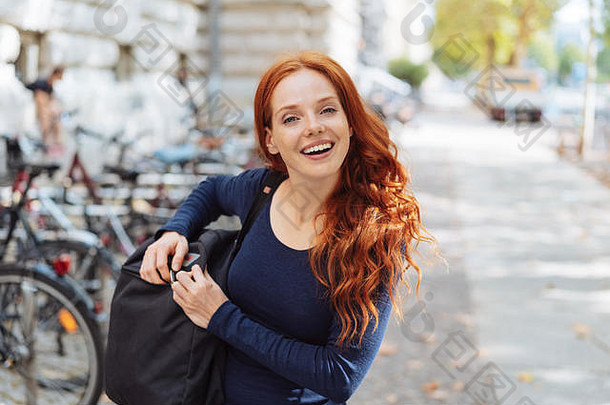年轻红发女子背着背包在街上行走的照片