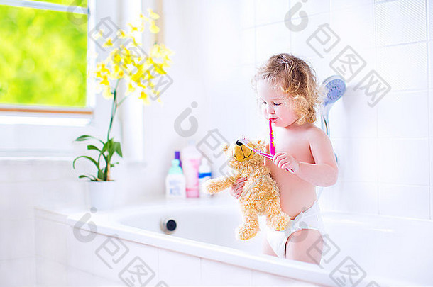 快乐有趣的婴儿女孩穿尿布刷牙牙齿玩泰迪熊玩具牙刷浴缸