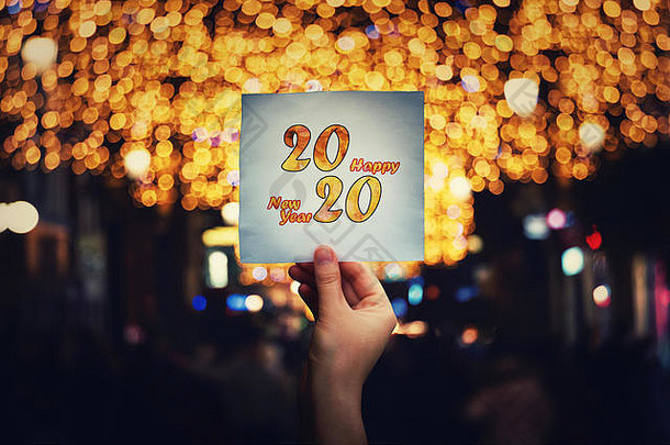 手持2020张新年贺词的纸在拥挤的夜街中间，圣诞灯和装饰不同。