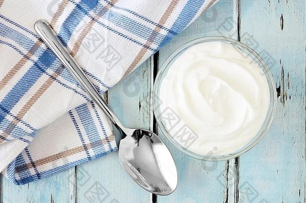 碗中的希腊酸奶，在质朴柔软的蓝色木材背景上，用布和勺子向下观看