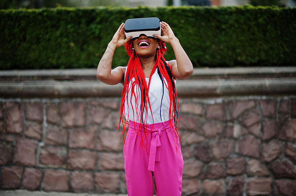 时尚的非裔美国女商人，穿着粉色裤子，戴着虚拟现实眼镜，穿着红色恐惧服。