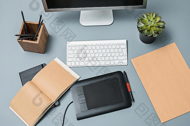 灰色的书桌上有笔记本电脑、空白纸记事本、花盆、手写笔和用于修饰的平板电脑